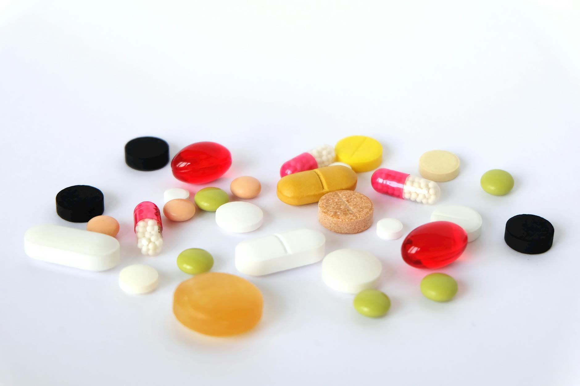 Verstreute bunte Pillen, Kapseln und Tabletten liegen auf weißem Untergrund.