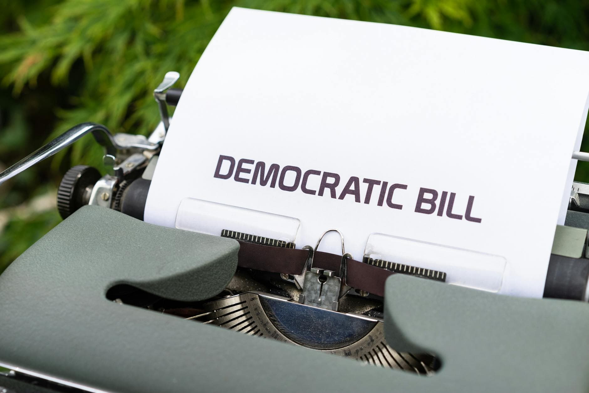 Eine Schreibmaschine mit einem Blatt Papier, auf dem DEMOCRATIC BILL steht, vor verschwommenem Grün.