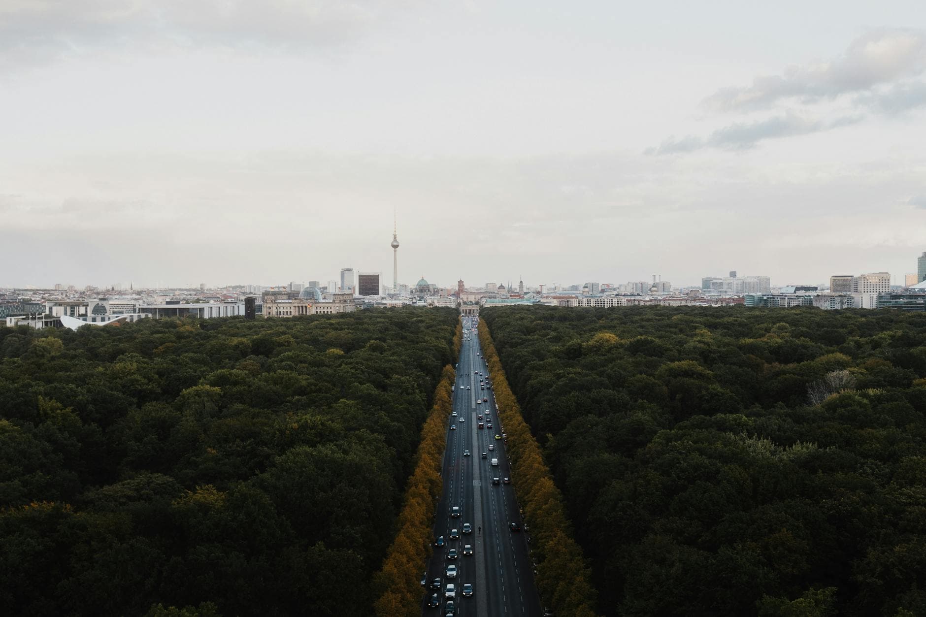 Luftaufnahme der Straße des 17. Juni durch den Tiergarten in Berlin mit Brandenburger Tor, Reichstag und Fernsehturm am Horizont.