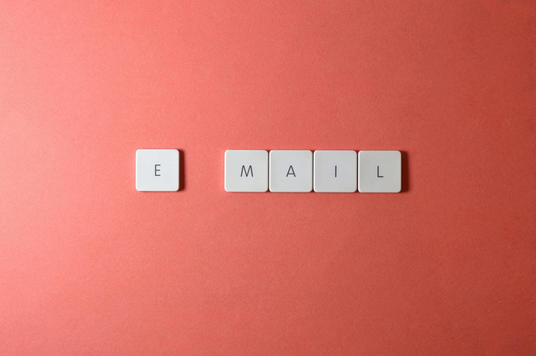Weiße Buchstabenkacheln bilden auf korallenfarbenem Hintergrund das Wort EMAIL.