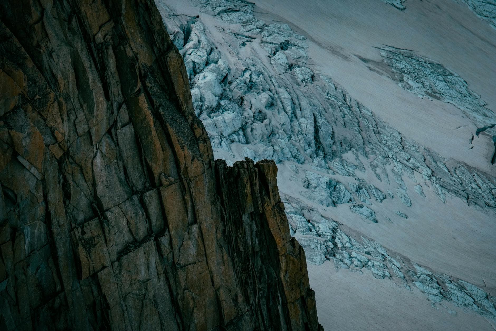 Zerklüftete, dunkle Felswand links grenzt an einen bläulich-weißen Gletscher mit zahlreichen Spalten rechts.