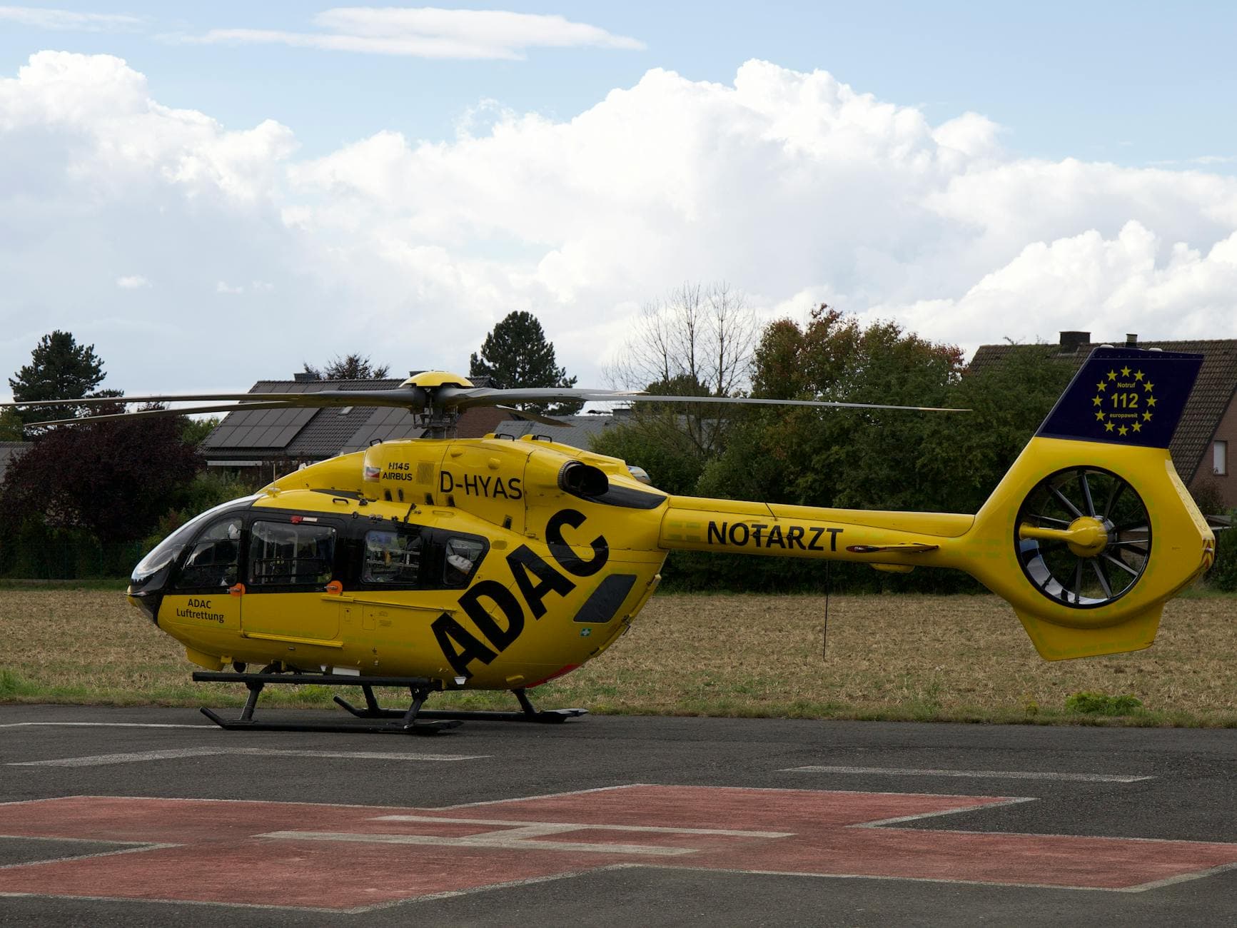 Gelber ADAC Notarzthubschrauber D-HYAS H145 auf Landeplatz, mit Hinweis Notruf 112 europaweit.