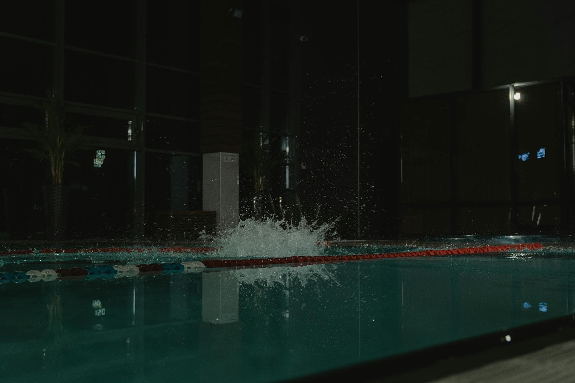 Großer Wasserspritzer in einem dunklen Schwimmbecken mit roten und blauen Bahnenleinen.
